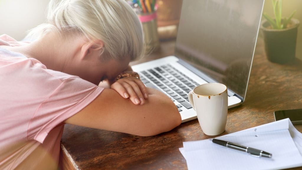 A woman sits down at her laptop, head down, attempting to write her LinkedIn About section