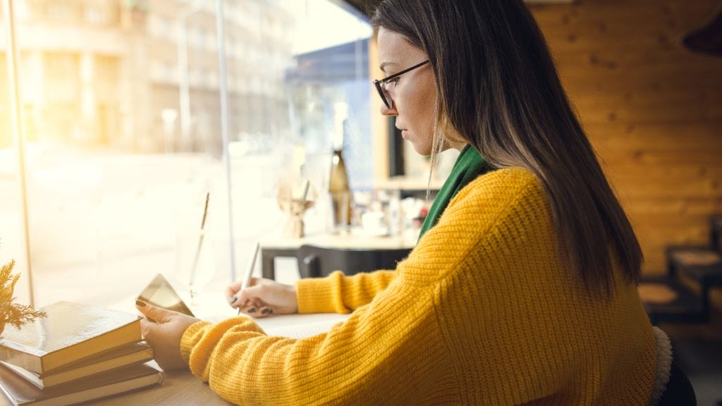 A woman in a yellow sweater writes and attempts to target her LinkedIn profile